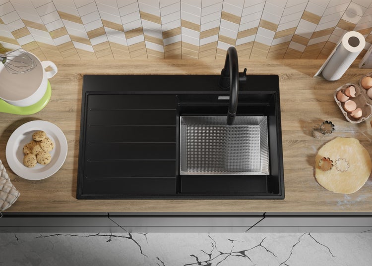 Schwarze Küchenspüle mit Abtropffläche auf einer Küchentheke mit Backutensilien.