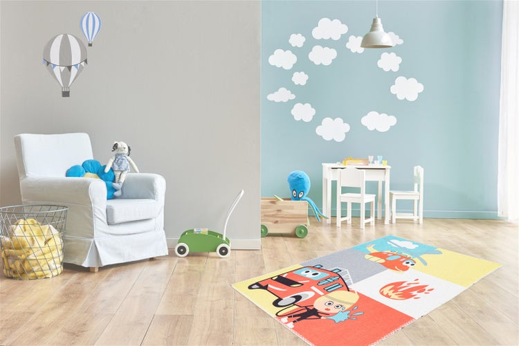 Helles, organisiertes Kinderzimmer mit Feuerwehr-Spielteppich, weißem Sessel, Kindertischgruppe aus Holz und Wandstickern auf Laminat.