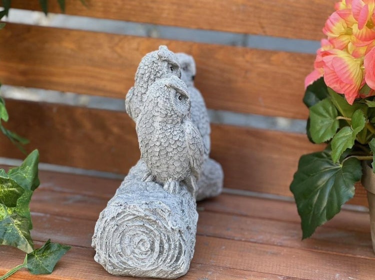 Zwei dekorative Eulenfiguren aus Steinguss sitzen auf einem Baumstamm als Gartenfigur.
