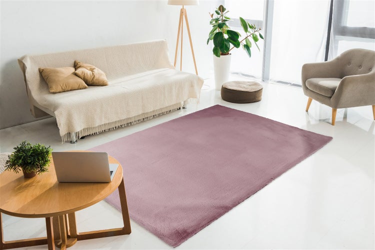 Moderner Wohnbereich mit lila Teppich, hellem Sofa, Holzcouchtisch, Sessel und Zimmerpflanzen in einem hellen, lichtdurchfluteten Raum.