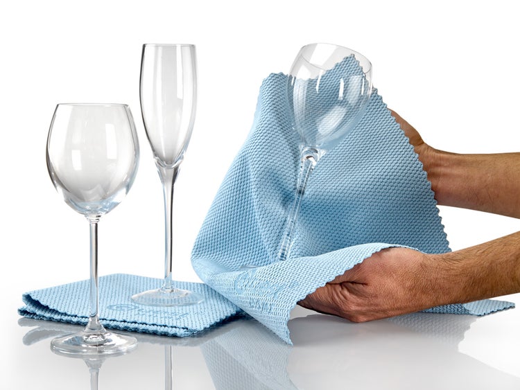 Ein Mann reinigt ein Weinglas mit einem blauen Reinigungstuch, im Hintergrund stehen zwei weitere Weingläser.