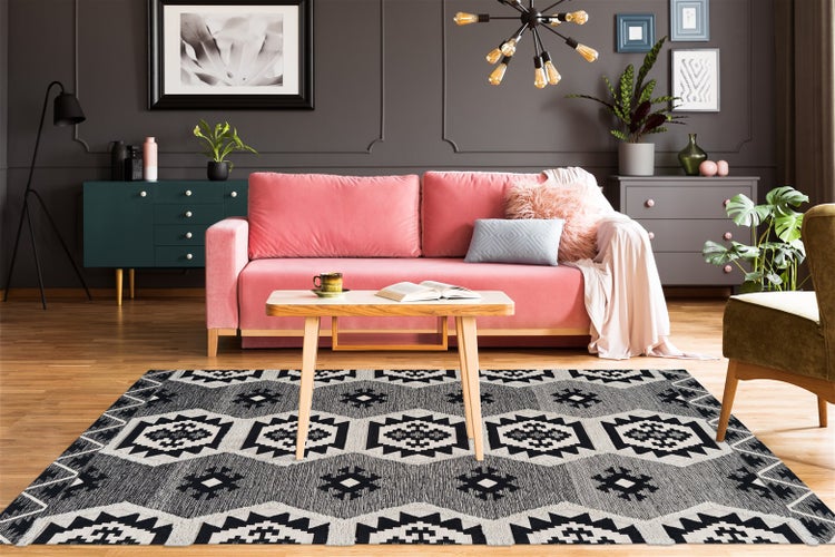 Modernes Wohnzimmer mit geometrisch gemustertem Teppich, rosa Sofa und Holztisch vor einer dunklen Wand mit Zierleisten.