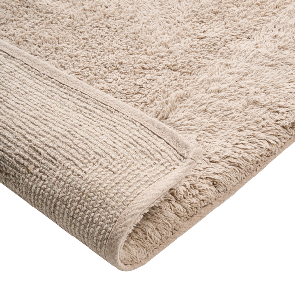 Nahaufnahme einer weichen, dicken Badematte in Beige mit strukturierter Oberfläche und eingefasstem Rand.