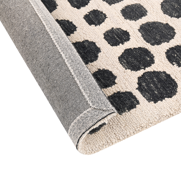 Teppich mit schwarzen Punkten auf hellem Grund, Detailansicht mit umgeknickter Ecke und Rückseite.