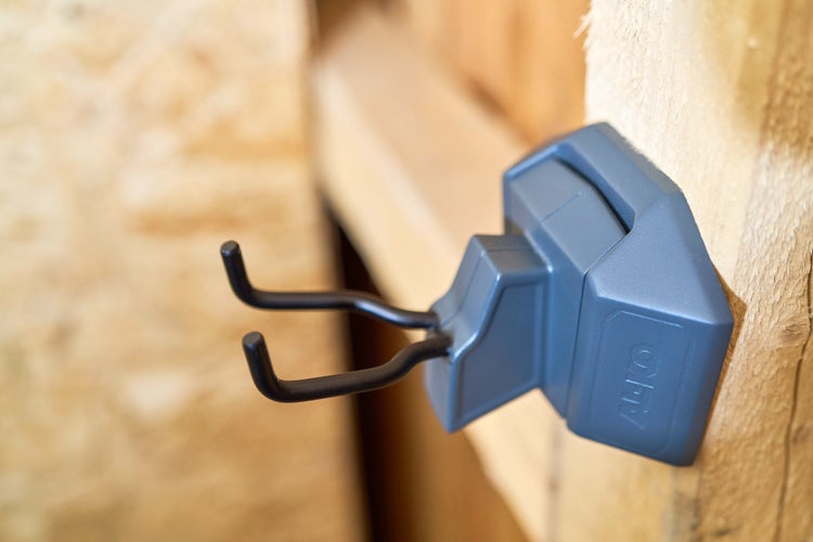 AL-KO Gerätehalter aus Kunststoff mit zwei Haken aus Metall an einer Holzwand montiert.
