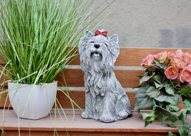 Gartenfigur Hund Yorkshire Terrier in Steinoptik auf einer Holzbank neben Topfpflanzen.