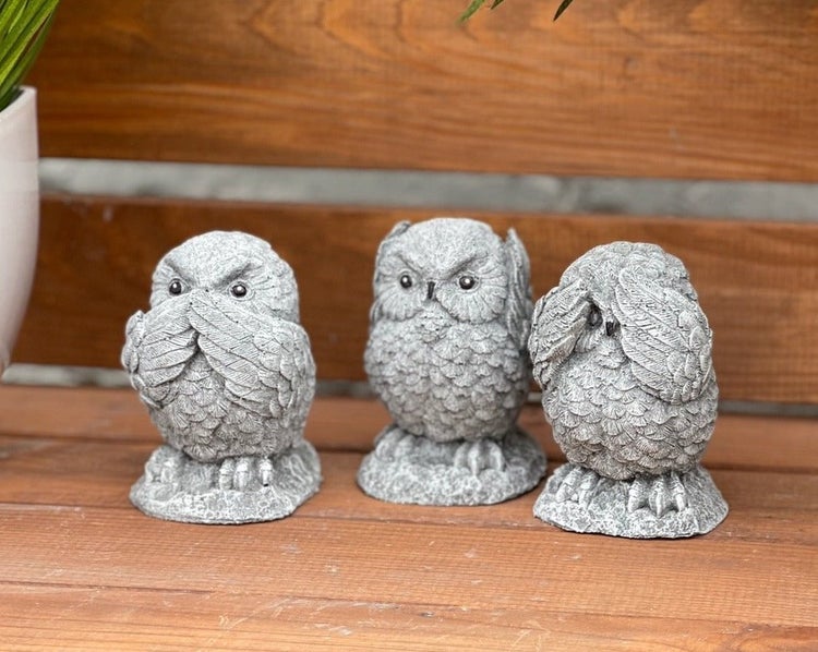 Drei Eulenfiguren aus Steinguss in unterschiedlichen Posen als Gartendeko auf Holzuntergrund.