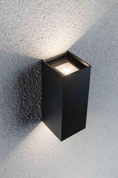 Moderne quaderförmige LED Wandleuchte für den Außenbereich mit Lichtaustritt nach oben und unten an einer strukturierten Wand.