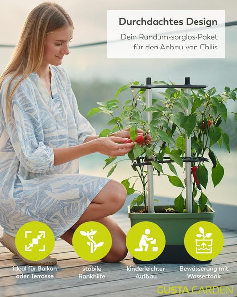 Frau erntet Chilis aus einem Chili-Anzuchtset auf einem Balkon oder einer Terrasse. Das Set beinhaltet eine Rankhilfe und einen Wassertank.