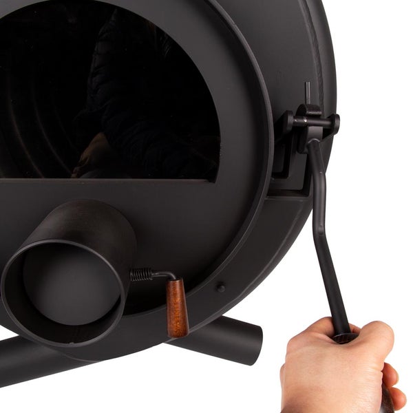 Detailansicht eines schwarzen Kaminofens mit Hand, die den Griff bedient