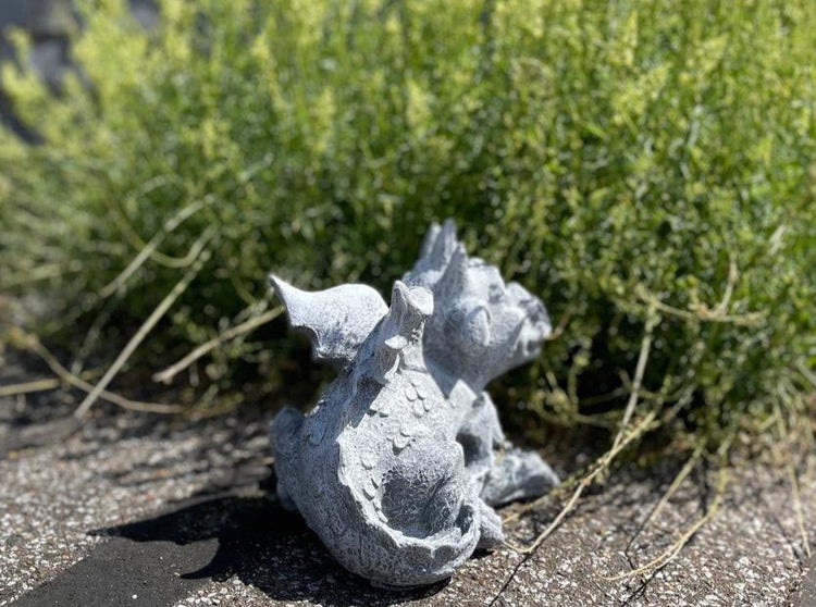 Dekorative Gartenfigur in Form eines kleinen Drachen aus Steinguss, platziert im Gartenbeet als dekoratives Element.