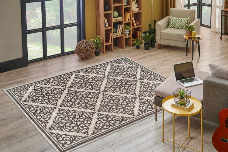 Rechteckiger Teppich mit Ornamentmuster in hellem Wohnzimmer mit Laminatboden, Bücherregal und Sessel. Modernes und organisiertes Ambiente.