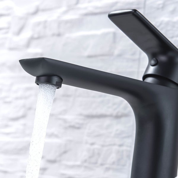 Schwarze Waschtischarmatur aus Metall mit fließendem Wasserstrahl vor einer hellen Strukturwand