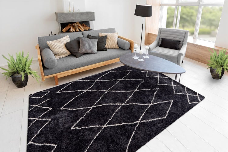 Schwarzer Shaggy Teppich mit weißem Rautenmuster in einem hellen, modern eingerichteten Wohnzimmer mit grauem Sofa und Sessel.