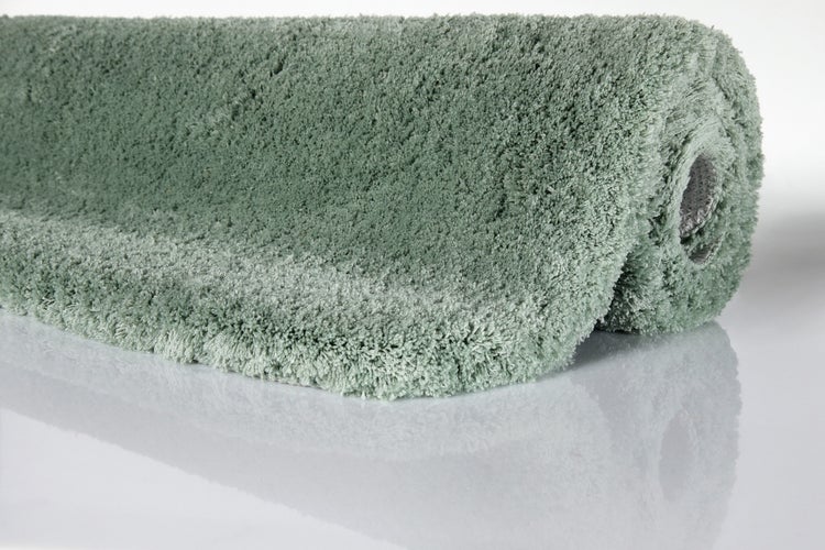 Grüner Hochflor-Teppich Shaggy, weiche Textur, aufgerollt.