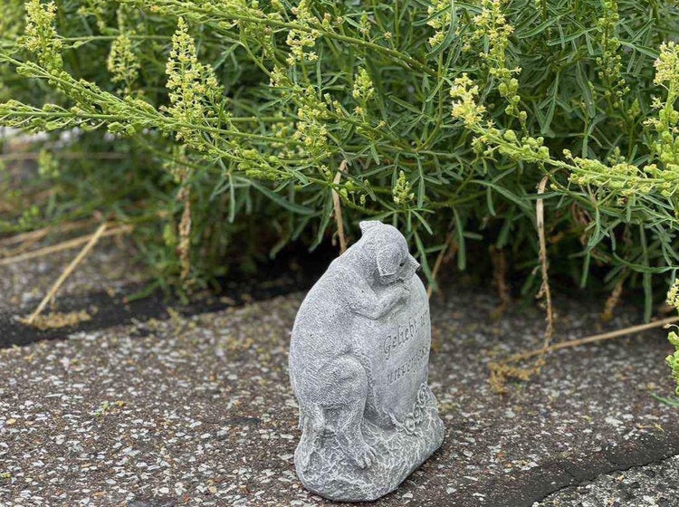 Grabschmuck in Form eines Hundes, der an einem Stein lehnt, für den Garten