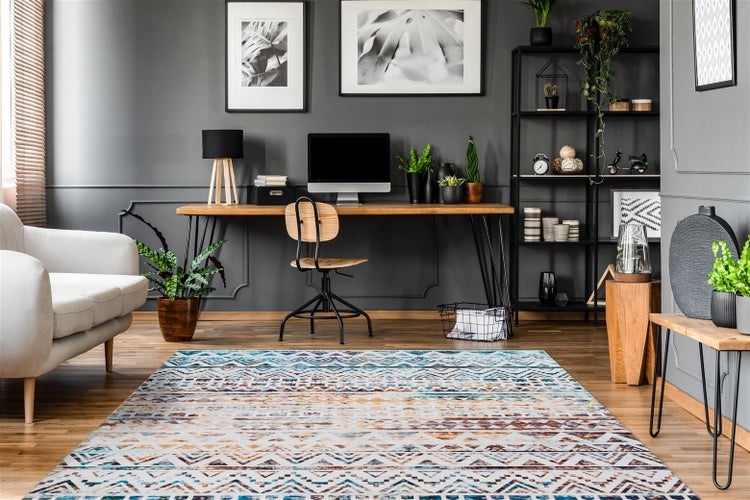 Modernes Arbeitszimmer mit geometrischem Teppich auf Holzfußboden, Holzschreibtisch mit Computer, Metallregal und weißem Sofa.