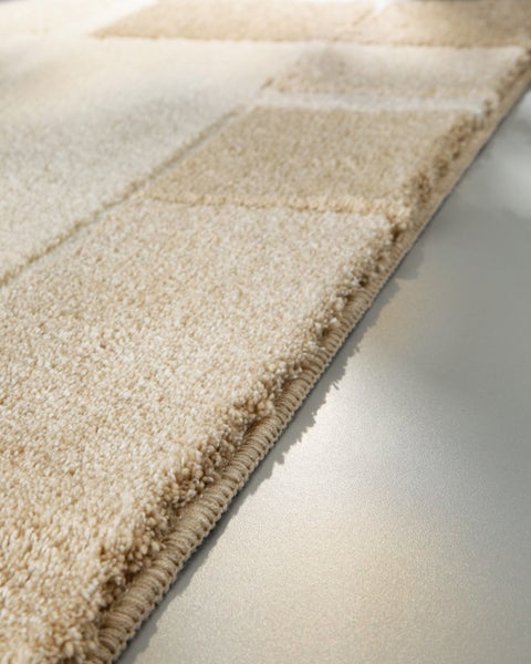 Nahaufnahme eines Hochflor-Teppichs mit geometrischem Reliefmuster und umkettelter Kante.