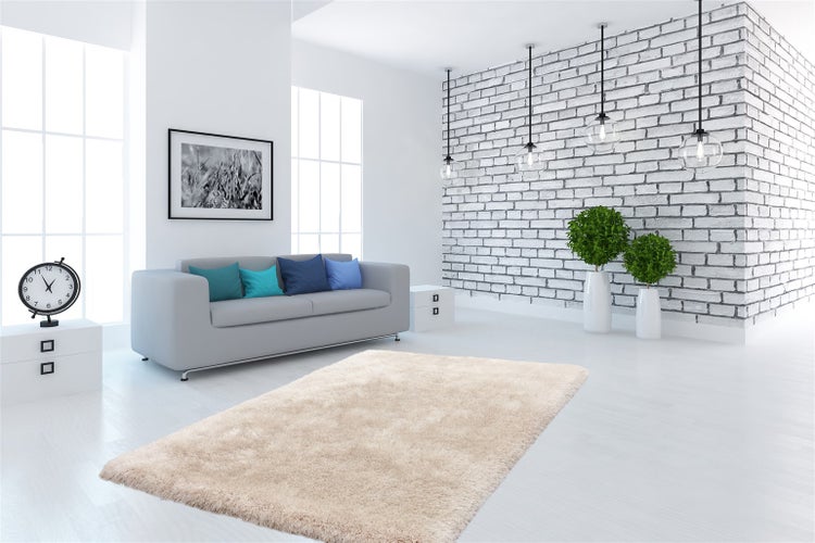 Modernes, helles Wohnzimmer mit flauschigem Teppich, grauem Sofa, weißer Ziegelwand, Pendelleuchten aus Glas und grünen Pflanzen.