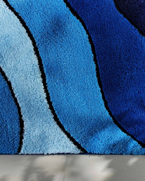 Detailaufnahme eines Hochflor-Teppichs mit Wellenmuster in verschiedenen Blautönen.