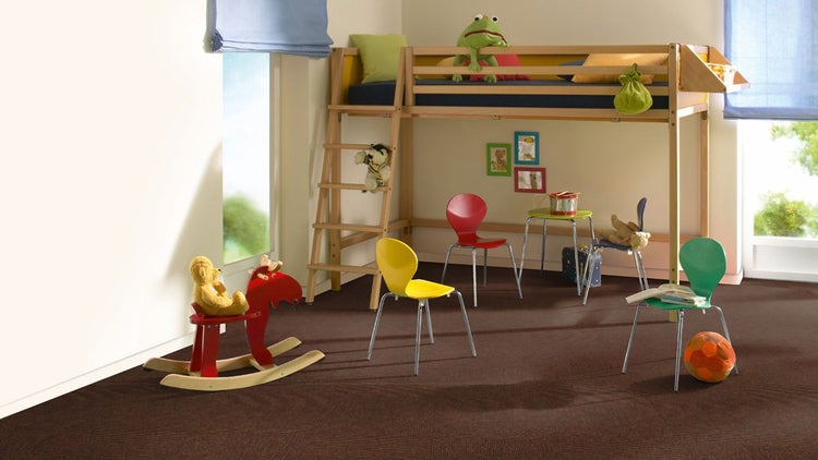 Hell beleuchtetes Kinderzimmer mit dunkelbraunem Teppichboden, einem Hochbett aus Holz, farbenfrohen Stühlen und einem roten Schaukelpferd.