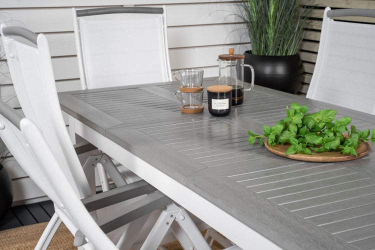 Szene mit einem Esstisch und Stühlen auf einer Terrasse, dekoriert mit Geschirr, Kerze und Kräutern