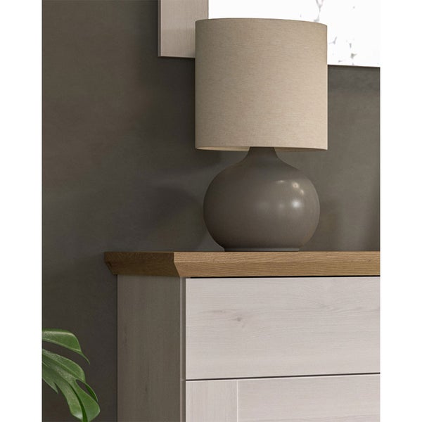 Moderne Tischleuchte mit rundem Fuß und Textilschirm auf einer Kommode mit Holzoberfläche.
