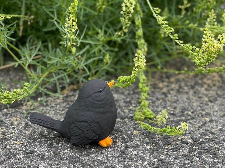Dekorative Gartenfigur in Form einer Amsel aus witterungsbeständigem Material auf einem Steinboden vor grünen Pflanzen.