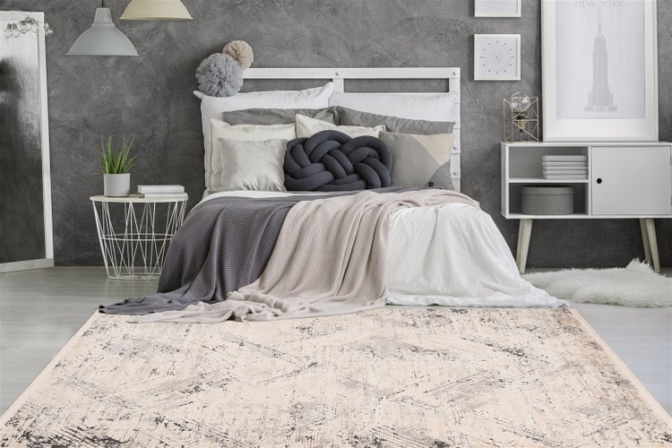 Moderner Teppich mit abstraktem Muster vor einem Bett im hellen Schlafzimmer mit grauer Wand, Beistelltisch und weißem Sideboard.