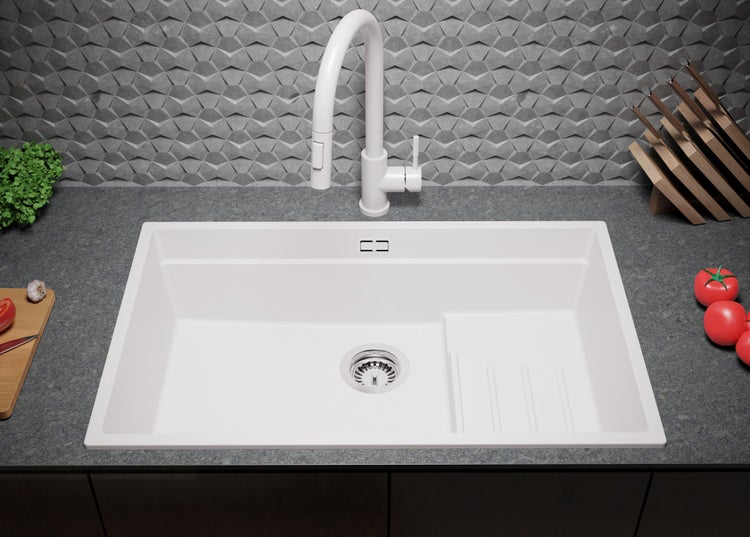 Weißes Spülbecken mit Abtropffläche und Armatur vor gemusterter Wand.