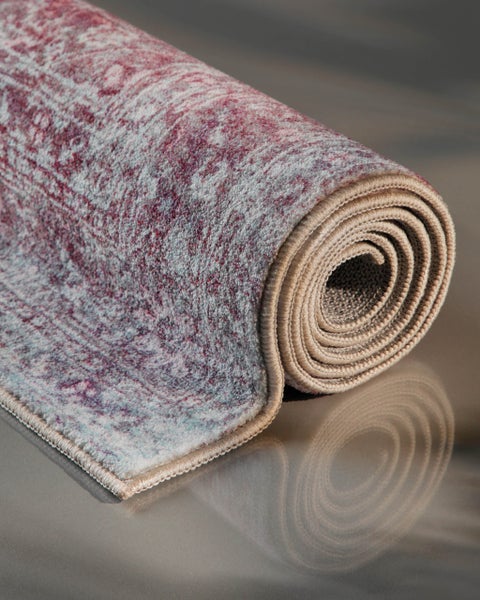 Zusammengerollter Teppich mit Vintage-Muster in Lila und Blau mit geketteltem Rand.