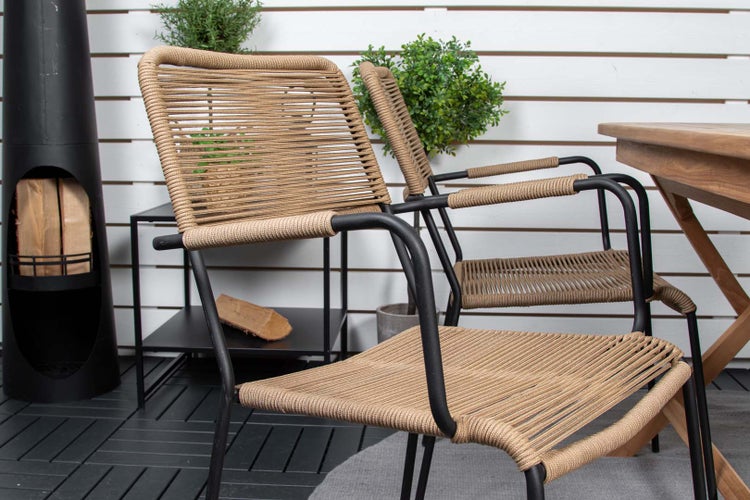 Terrassenszene mit zwei Stühlen mit Seilbespannung und schwarzem Metallrahmen, einem Beistelltisch, einem Kaminofen und einem Holztisch