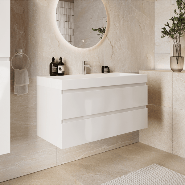 Wandhängender weißer Waschtischunterschrank mit zwei Schubladen und Waschbecken, helles Badezimmer in Steinoptik mit rundem Leuchtspiegel.