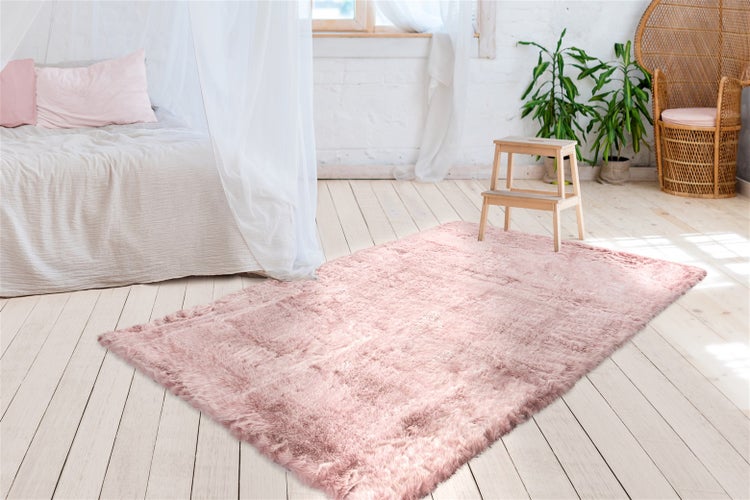 Flauschiger rosa Hochflor-Teppich in einem hellen Schlafzimmer mit Holzboden, Himmelbett und Zimmerpflanzen.