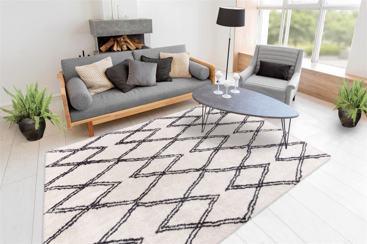 Heller Teppich mit schwarzem Rautenmuster in einem modern eingerichteten Wohnzimmer mit grauem Sofa und Couchtisch.