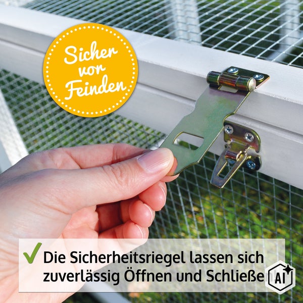Eine Hand öffnet einen metallenen Sicherheitsriegel an einem Kleintierstall aus Holz mit Drahtgitter und Schutz vor Fressfeinden.