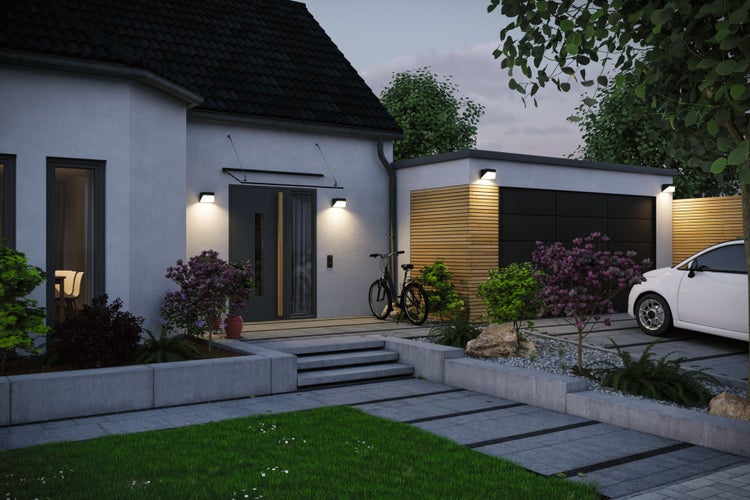 Moderne Hausfassade mit beleuchtetem Hauseingang und Garage in der Abenddämmerung bei Gartenbeleuchtung