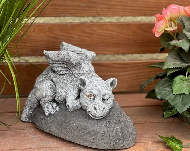 Gartenfigur Drache aus Steinguss, liegend auf einem Stein mit Flügeln und einem zwinkernden Auge.
