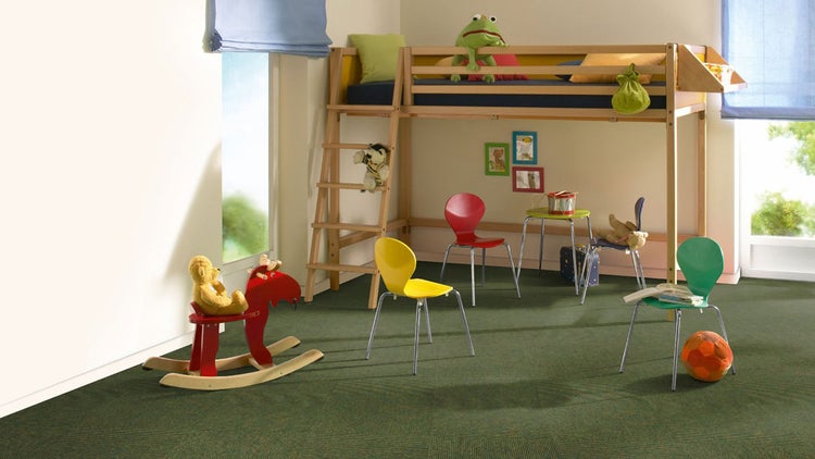 Helles Kinderzimmer mit hölzernem Hochbett, bunten Stühlen und grünen Teppichfliesen.