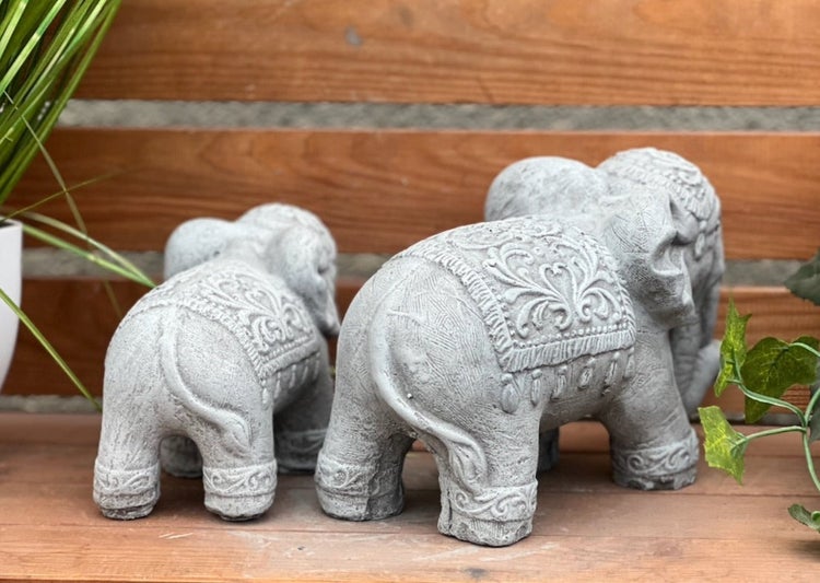 Drei detailliert verzierte Gartenfiguren in Elefantenform aus Steinguss in verschiedenen Größen auf einer Holzoberfläche.