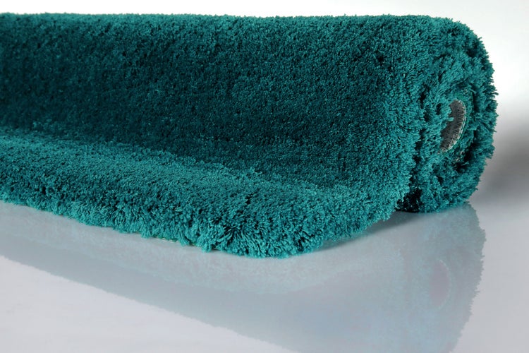Türkisfarbener Hochflor-Teppich Shaggy, weiche und flauschige Textur, eingerollt.