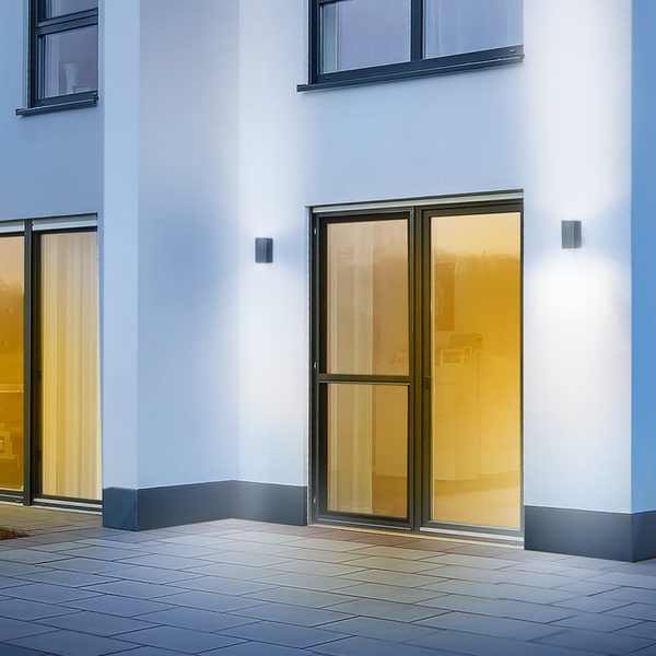 Moderne Außenwandleuchten an einer hellen Hausfassade mit Terrasse und Terrassentüren bei Beleuchtung.
