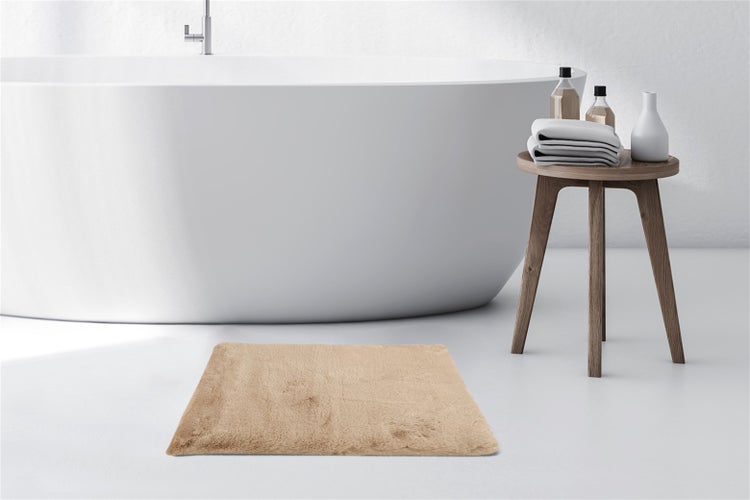 Rechteckige, flauschige Badematte in einem hellen Badezimmer neben einer freistehenden Badewanne und einem Holzhocker mit Handtüchern.