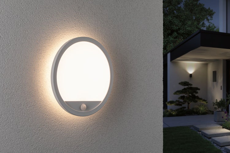 Runde LED Außenwandleuchte mit Bewegungsmelder an einer Hausfassade montiert, strahlt warmes Licht aus.