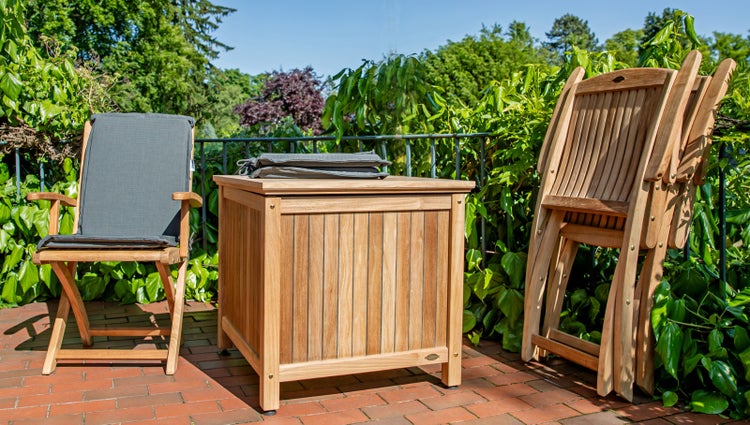 Gartenszene mit Holzgartenmöbeln, bestehend aus Klappstühlen, einem Stuhl mit Polster und einer Aufbewahrungsbox