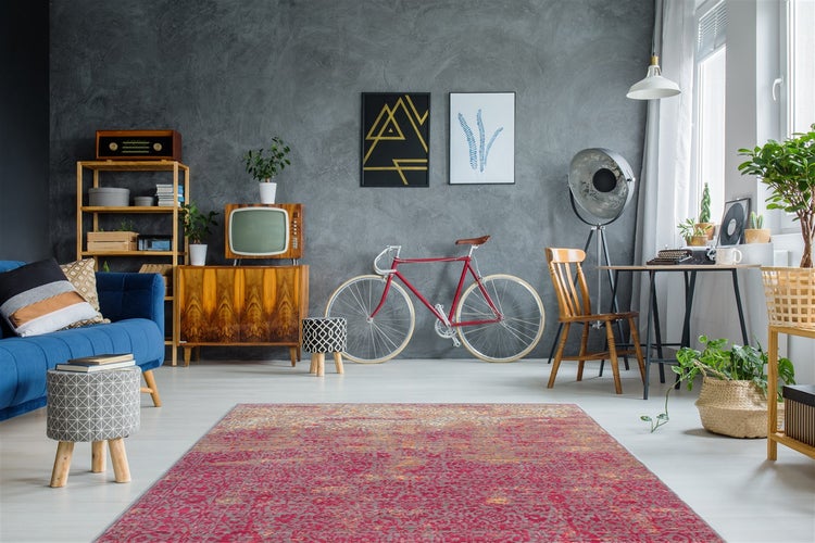 Hell eingerichtetes Wohnzimmer mit rotem Vintage-Teppich, dunkelgrauer Wand, Holzmöbeln, blauem Sofa und einem Fahrrad.