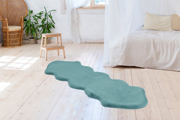 Langflor-Teppichläufer in Türkis mit Wellenrand auf hellem Holzboden in einem hellen Schlafzimmer mit Korbsessel und Pflanzen.