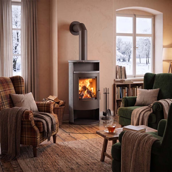 Ein moderner Kaminofen mit Sichtfenster in einem gemütlichen Wohnzimmer vor einem verschneiten Fenster. Der Ofen brennt und verbreitet Wärme.