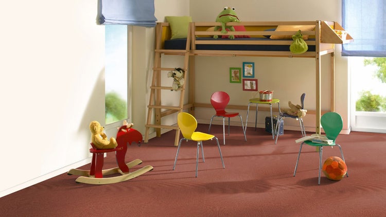 Helles Kinderzimmer mit rotbraunen Teppichfliesen, einem Hochbett aus Holz, bunten Stühlen und einem Schaukelpferd.