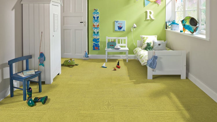 Helles Kinderzimmer mit strukturierten Teppichfliesen im Schachbrettmuster, Bett, Schrank und maritimer Dekoration.